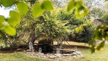 Een tuin met een stenen fontein, omringd door bomen en een houten constructie.