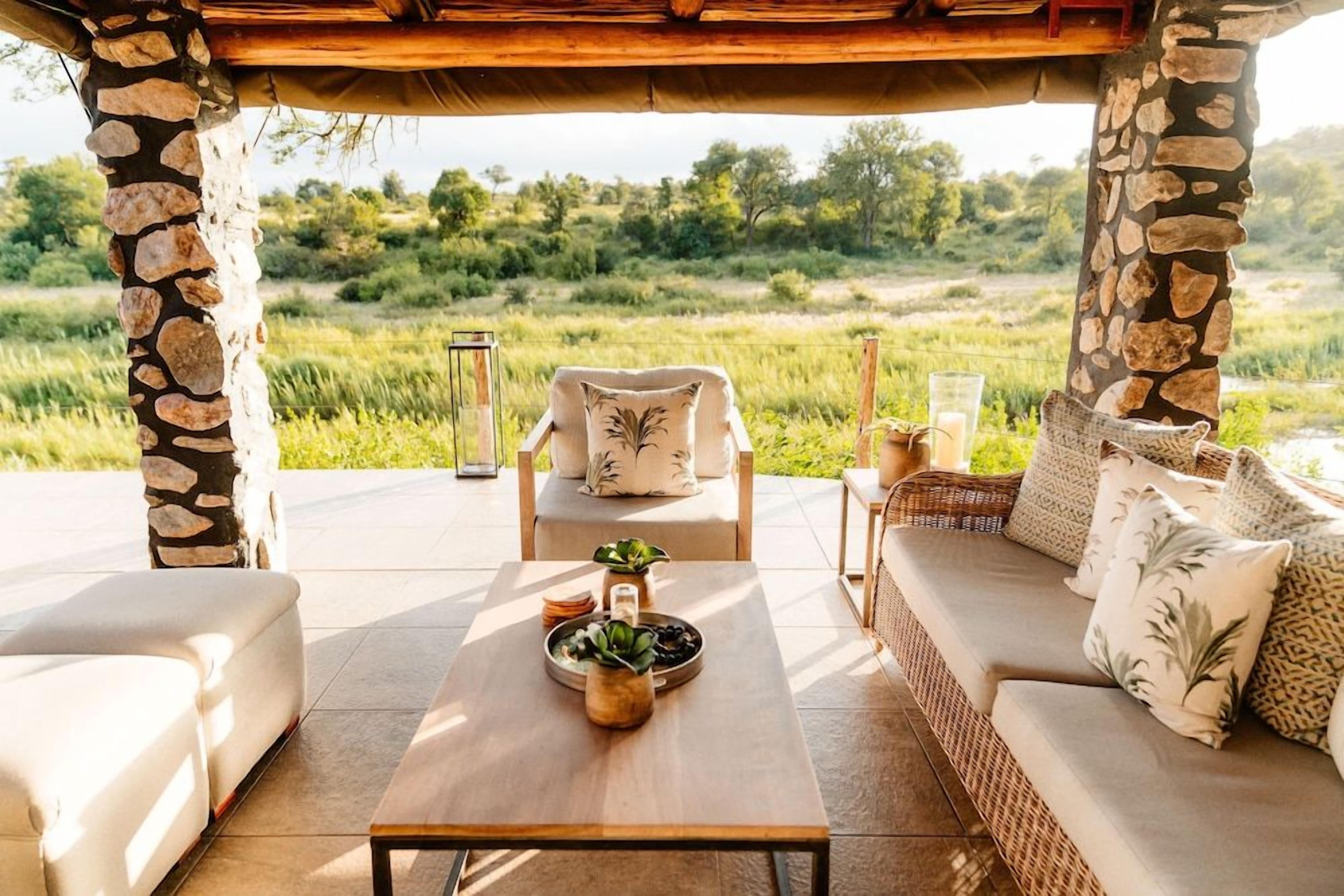 An outdoor seating area with stone pillars, a wooden table, and a wicker sofa.
