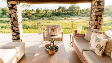An outdoor seating area with stone pillars, a wooden table, and a wicker sofa.