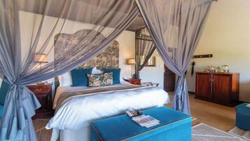 A bedroom with a four-poster bed, a nightstand, a dresser, and a blue ottoman.