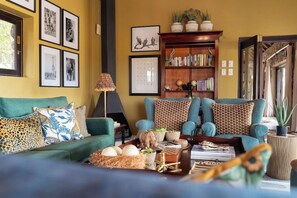 A living room with a sofa, armchairs, a bookshelf, and a fireplace. - Last Word Kitara Camp (Mpumalanga)