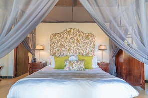 Een slaapkamer met een hemelbed, twee nachtkastjes met lampen en een hoofdeinde met bloemenprint.