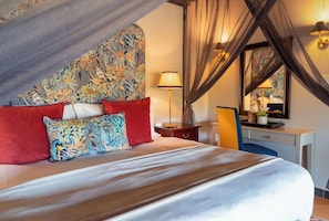 Een slaapkamer met een groot bed, een bureau, een stoel, een lamp en een spiegel.
