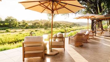 Een terras met stoelen en parasols, met uitzicht op een grasrijk landschap.