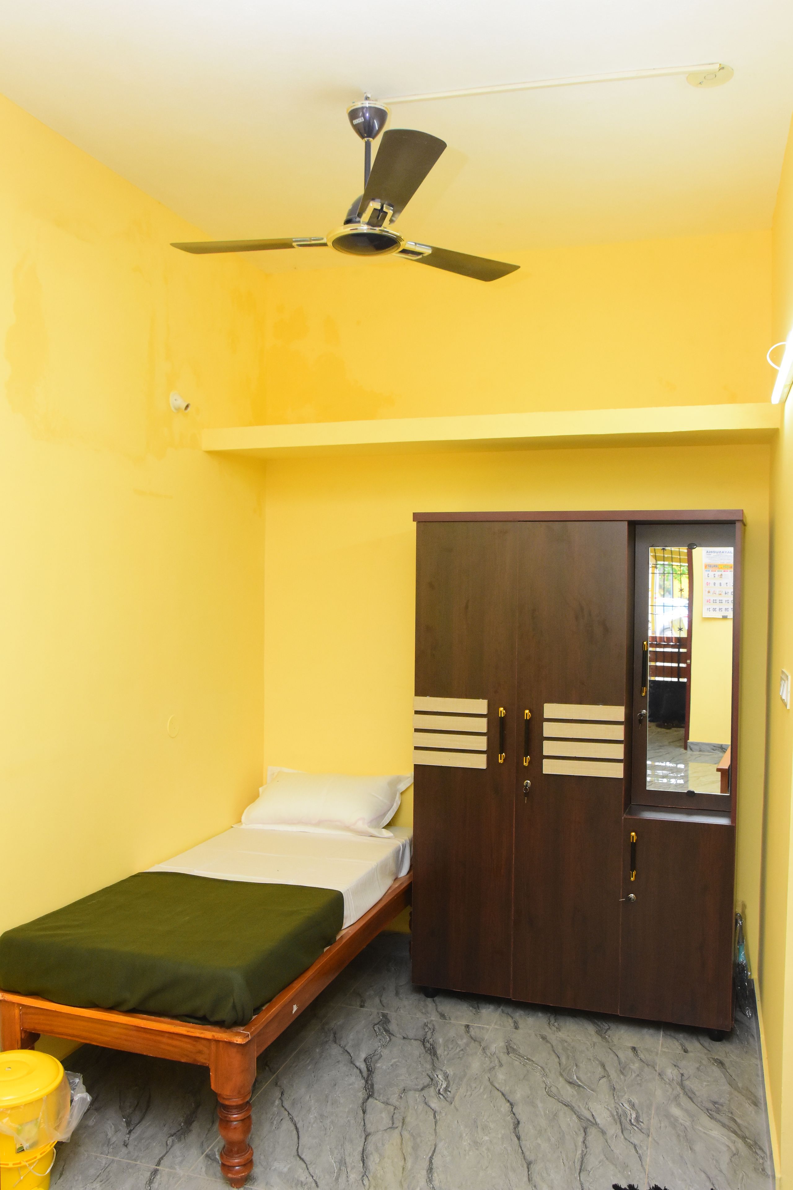 A room with a bed, a wardrobe, a ceiling fan, and a yellow wall.