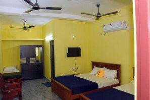Ein Zimmer mit zwei Betten, einem Schreibtisch und einem Stuhl. Es gibt Deckenventilatoren und eine Klimaanlage.