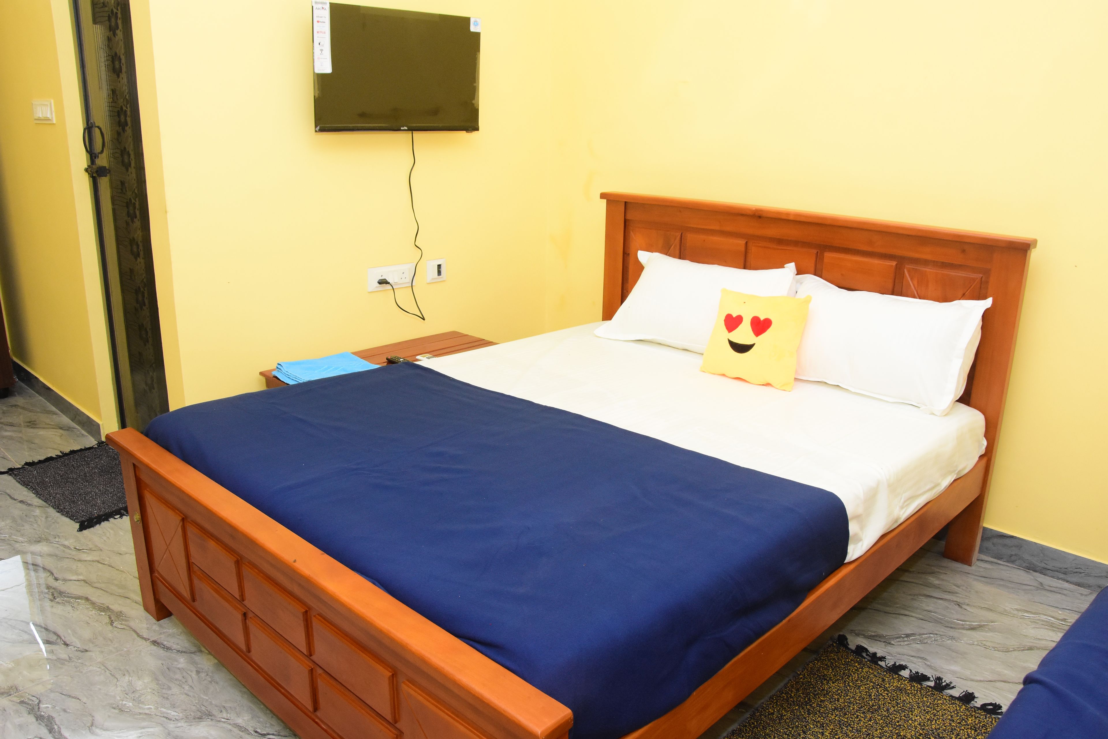 Un lit simple avec une tête de lit en bois, une couvre-lit bleue et un oreiller orné d’un motif en forme de cœur.