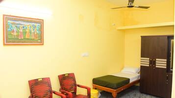 A room with a bed, two chairs, a ceiling fan, a wall-mounted light, and a framed picture.