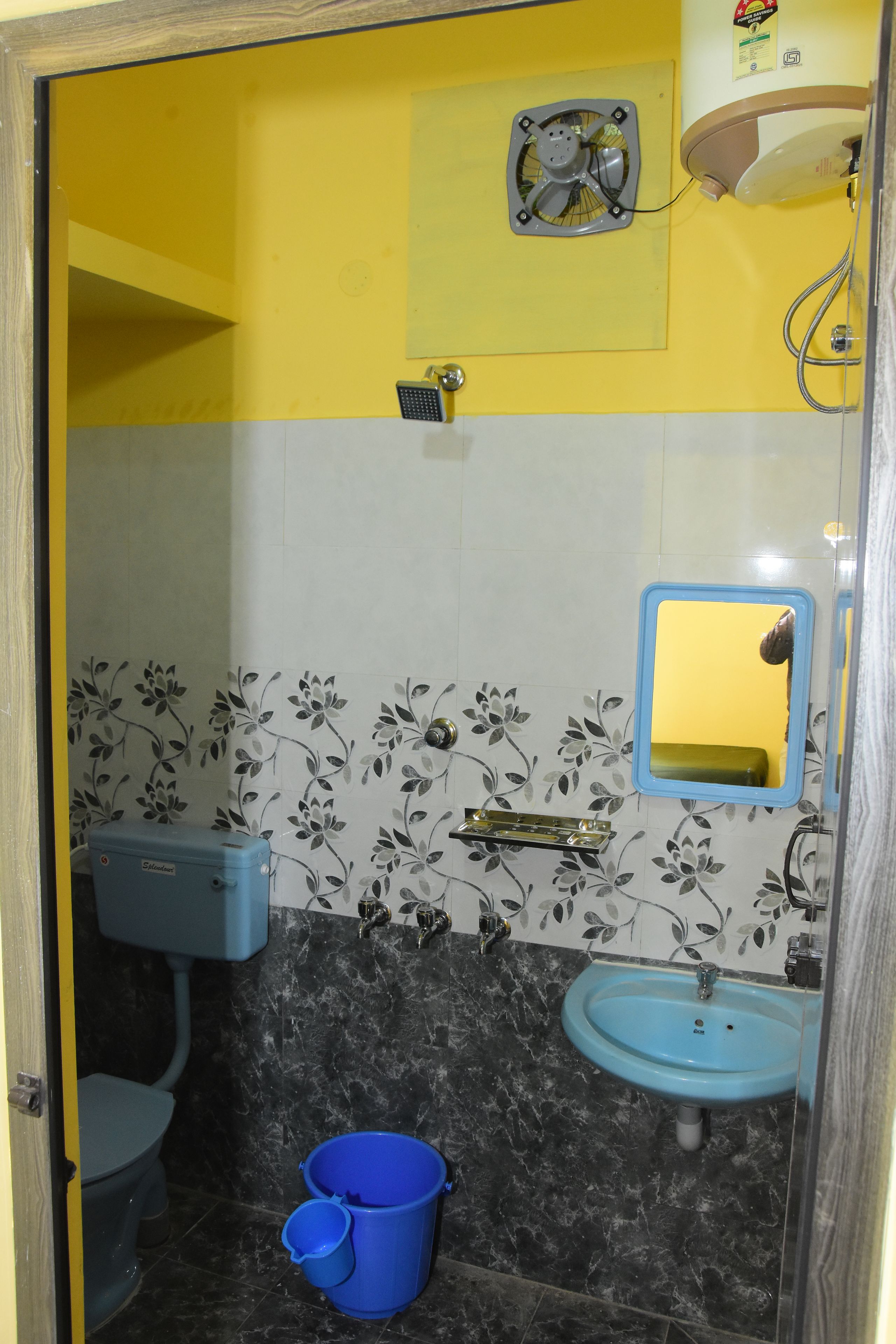 Un baño con inodoro, lavamanos y ducha. Hay un cubo azul y un espejo en la pared.