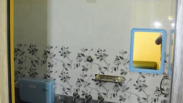 Un baño con inodoro, lavamanos y ducha. Hay un cubo azul y un espejo en la pared.
