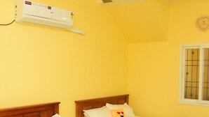 Et værelse med to senge i træ, en ventilator i loftet, en aircondition samt et vindue med tremmer.