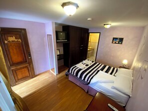 Un dormitorio con cama, televisión, puerta de madera y baño visible a través de una puerta abierta.