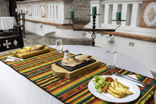 Una mesa de comedor con una comida que incluye pescado a la parrilla, papas fritas y ensalada, sobre un mantel colorido.