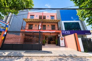 Un edificio de dos pisos con un acceso cubierto y un letrero que dice 'Kopi Cerita Setiap Hari'.