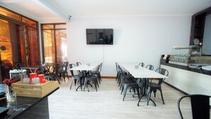 A dining area with a long table and chairs, a television mounted on the wall, and a counter with a display case. - Rehat at Zeva Guest House (Bandung)