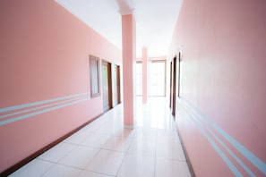 A corridor with pink walls, white tiled floor, and doors with numbers. - Rehat at Zeva Guest House (Bandung)