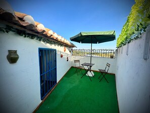 A small patio with a green artificial turf, a blue gate, and a table with chairs.