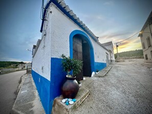 A building with a blue and white facade, a large arched entrance, and a potted plant with stones. - Holiday Home 'Alojamiento Rural La Tinaja' with Mountain View, Private Pool and Wi-Fi (Moriscote)