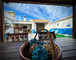 A rustic outdoor seating area with a woven basket on a wooden table, overlooking a traditional building with a tiled roof and a blue and white facade. - Holiday Home 'Alojamiento Rural La Tinaja' with Mountain View, Private Pool and Wi-Fi (Moriscote)