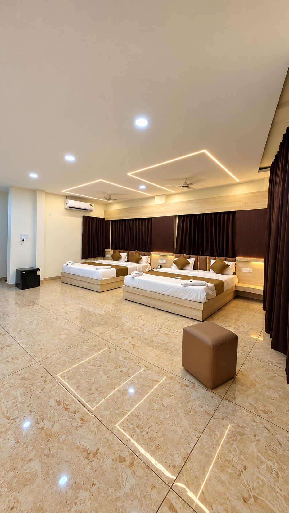 A hotel room with a large bed, a bedside table, a nightstand, a wardrobe, an air conditioning unit, and a ceiling fan.
