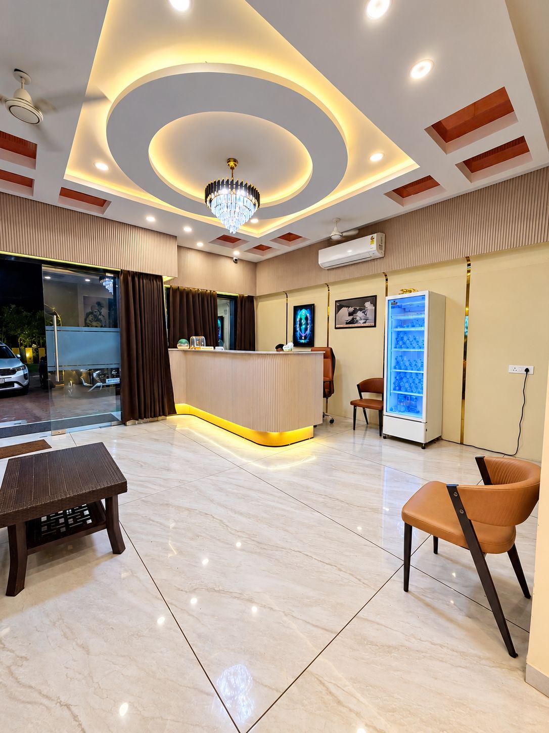 Een hotel receptie met een receptiebalie, zitplaatsen, een kroonluchter en een koelkast.