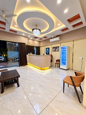 Zona de recepción de un hotel con mostrador, asientos, candelabro y refrigerador.