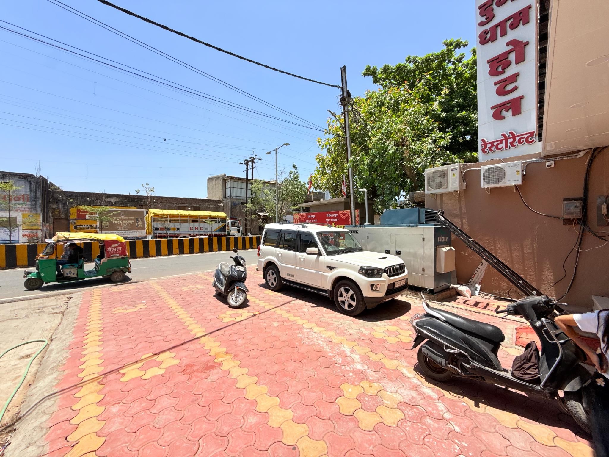 Una superficie pavimentada con una camioneta SUV blanca estacionada, una motocicleta y un auto-rickshaw verde.