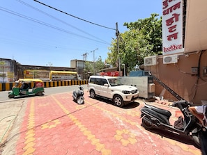 Una zona pavimentada amb un cotxe SUV blanc, una moto i un auto-rickshaw verd.