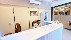 Un mostrador de recepción con un hombre sentado, un cuadro en la pared y un dispensador de agua.