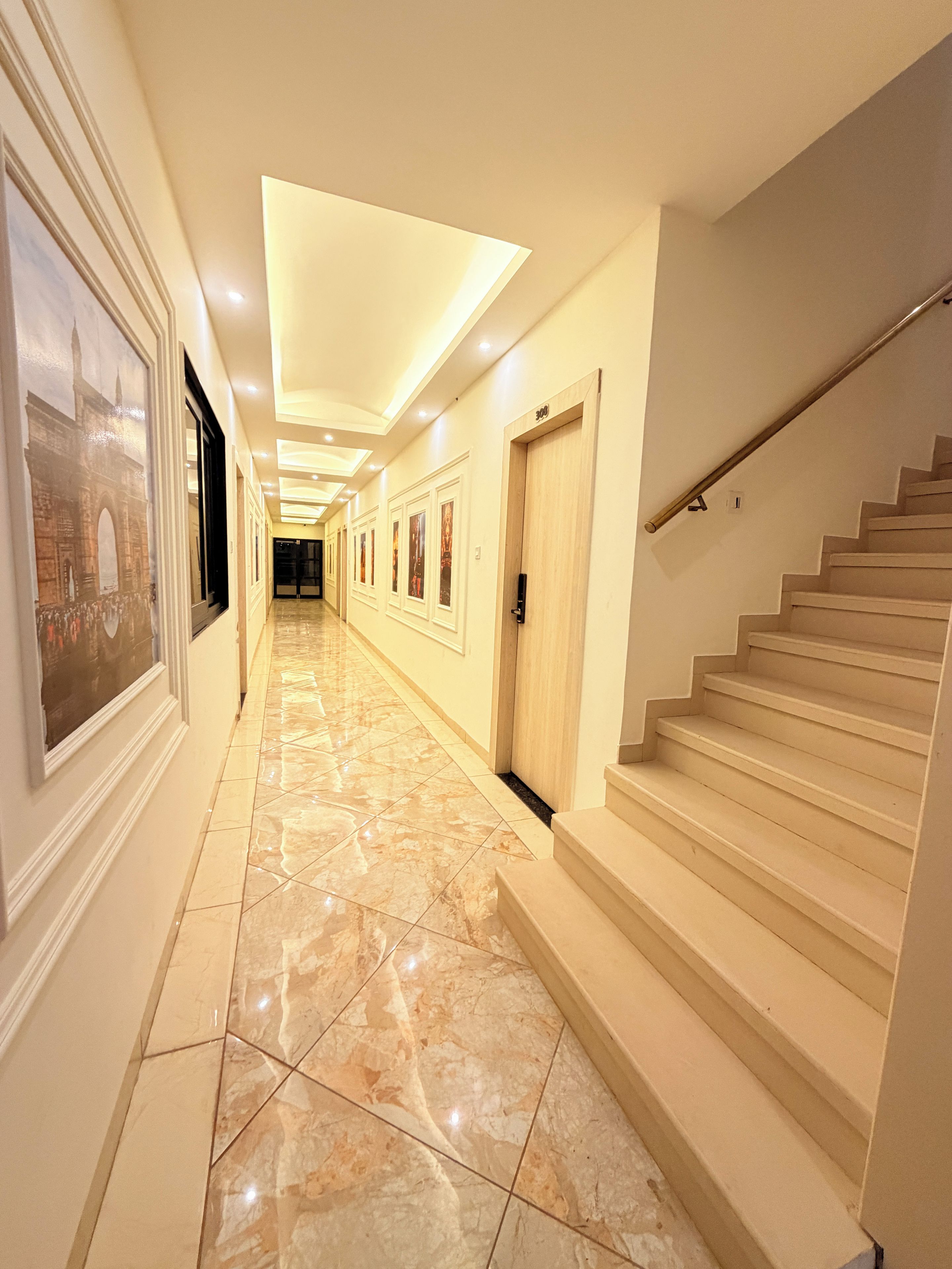 A hotel hallway with a marble floor, a staircase, and doors with artwork.