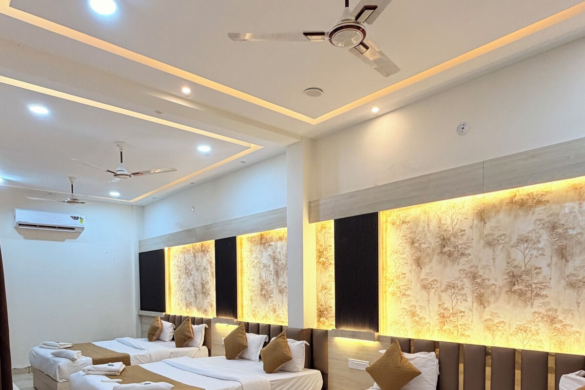Habitación de hotel con cuatro camas, ventiladores de techo, iluminación empotrada y un amplio mural en la pared.