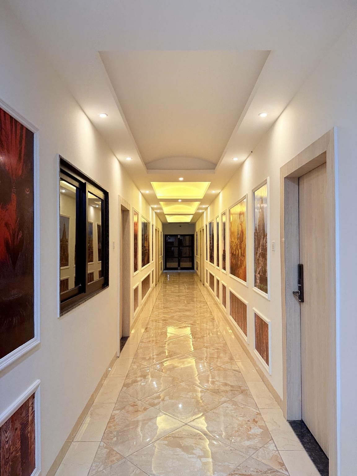 A long, narrow hallway with a polished floor, framed artwork on the walls, and recessed lighting.