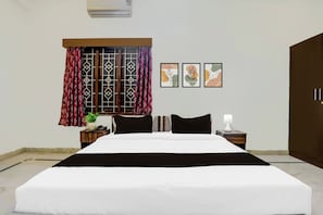Una habitación de hotel con una cama grande, una mesita de noche con lámpara, un teléfono y una planta en maceta.