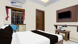 Ein Hotelzimmer mit Bett, Schreibtisch, Stuhl, einem an der Wand befestigten Fernseher und einer Klimaanlage.