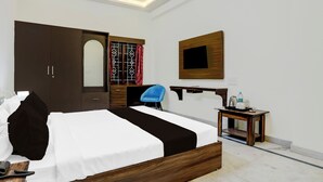 Ein Hotelzimmer mit einem Bett, einem Schreibtisch mit Stuhl, einem Kleiderschrank, einem Spiegel und einem an der Wand befestigten Fernseher.