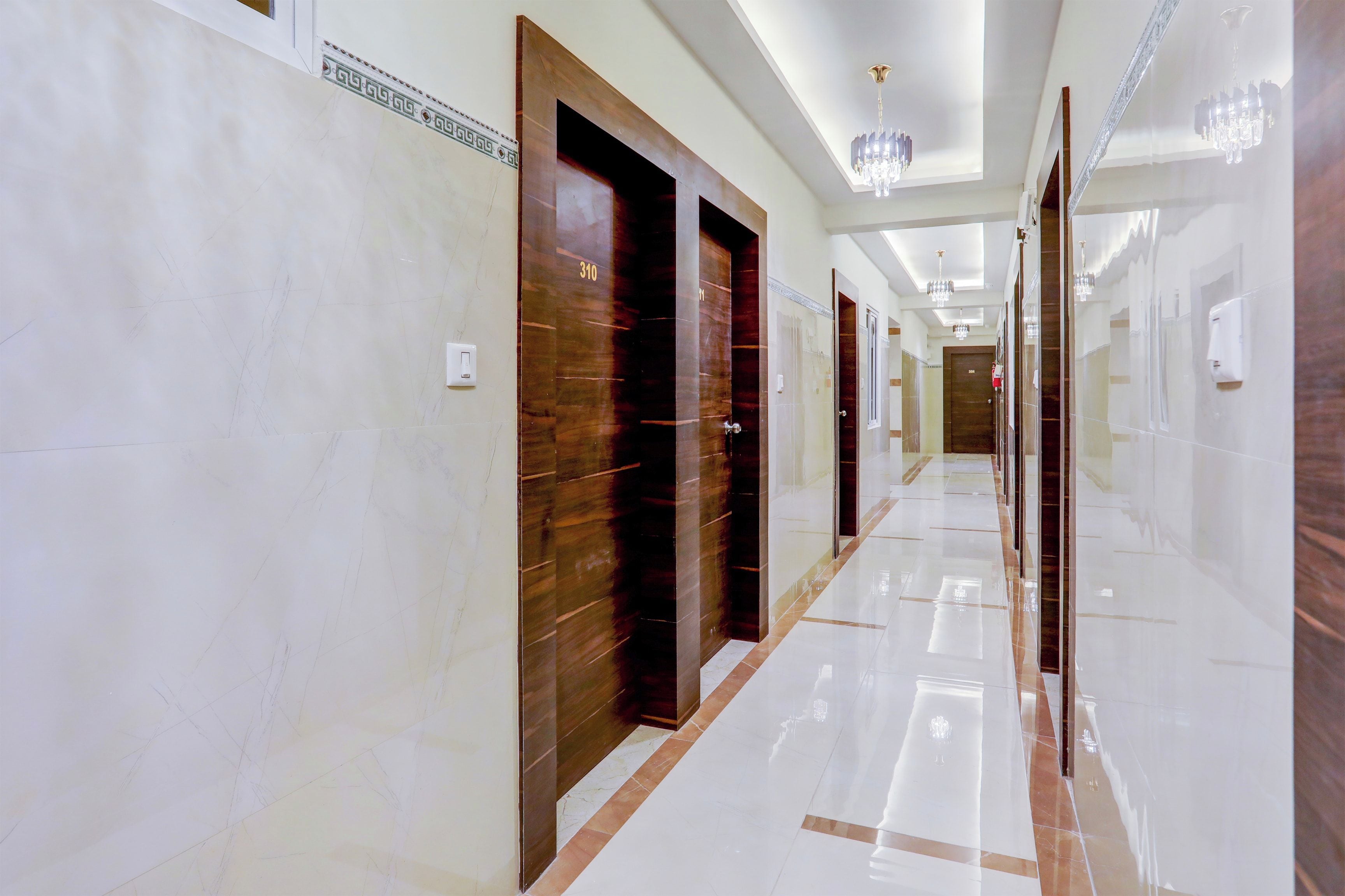 A hotel corridor with marble flooring, wooden doors, and modern chandeliers.