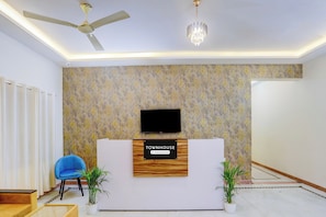 A reception area with a modern design, including a reception desk, a ceiling fan, a chandelier, and decorative wallpaper. - Townhouse Madiwala Lake Park (Bengaluru)