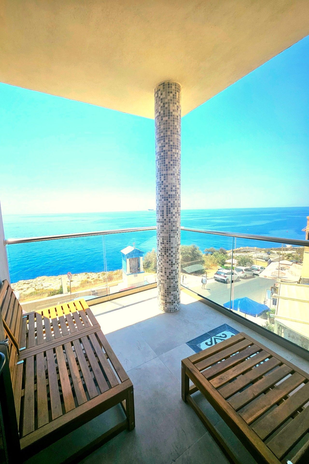 Un balcone con mobili in legno, una colonna in maiolica e vista sul mare e sugli edifici.