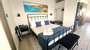 Una camera da letto con un letto, comodini, una panca, un quadro e vista sulla città.