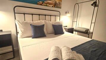 A hotel room with a bed, a painting of a coastal scene, a nightstand, a lamp, and a folded towel on the bed.
