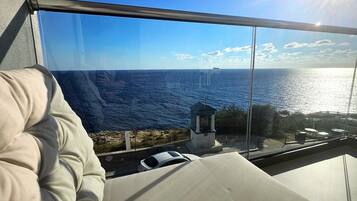 A room with a view of the sea, a bed, and a small structure in the distance.