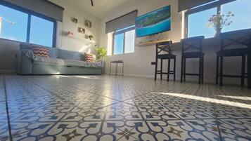 Un salon avec un sol à motifs, un canapé, un téléviseur et un coin repas avec des chaises.