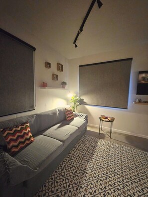A living room with a grey sofa, patterned rug, and a small side table. - Modern Blue Horizon Studio In Blue Grotto (Qrendi)