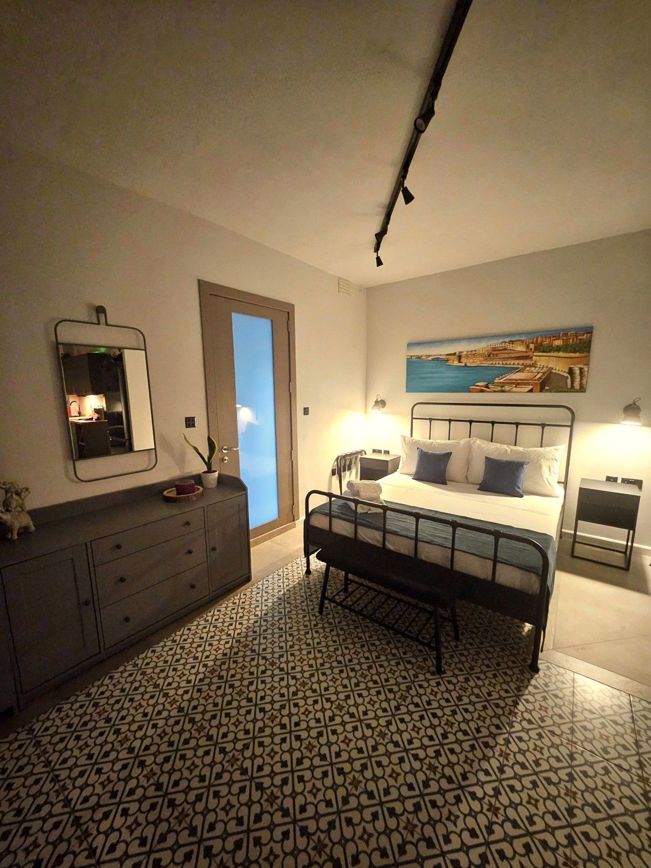 Une chambre à coucher avec un lit, des tables de chevet, une commode, un miroir et un sol à motifs.