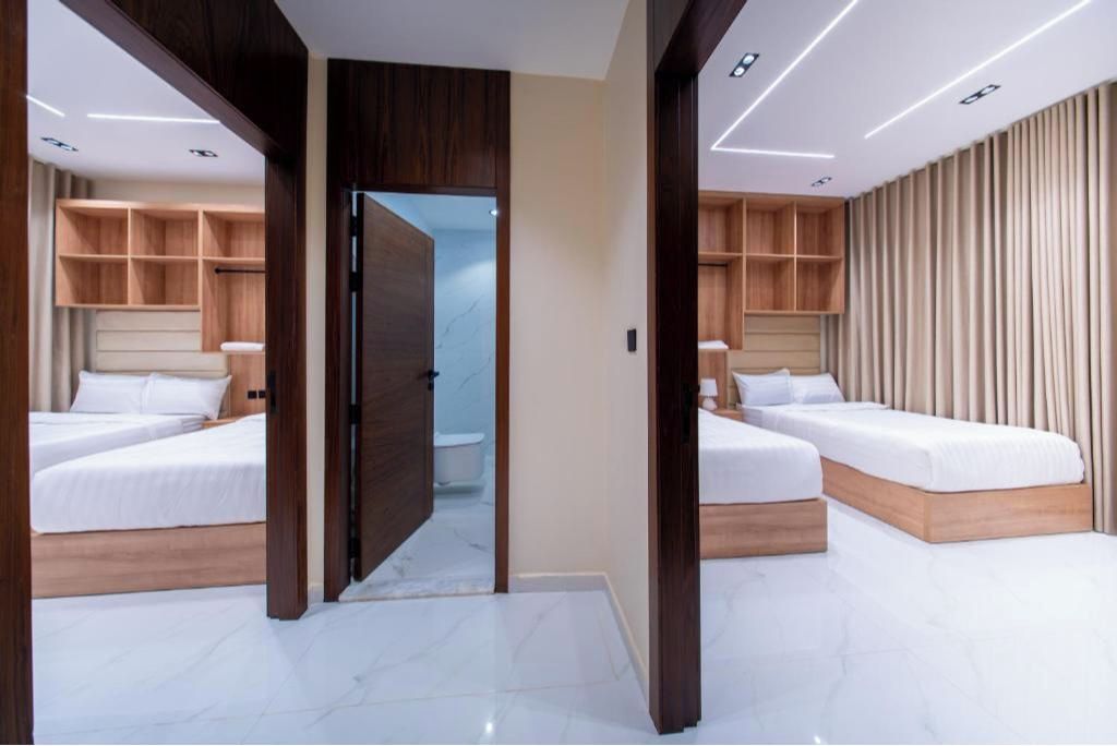 A modern hotel room with two beds, a walk-in closet, and a bathroom visible through an open door.