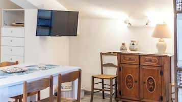 Ein Essbereich mit Tisch, Stühlen, einem Schrank, einem an der Wand befestigten Fernseher und einer Lampe.