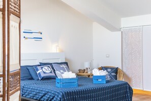 Quarto com cama, travesseiros, mesa de cabeceira, luminária e janela.