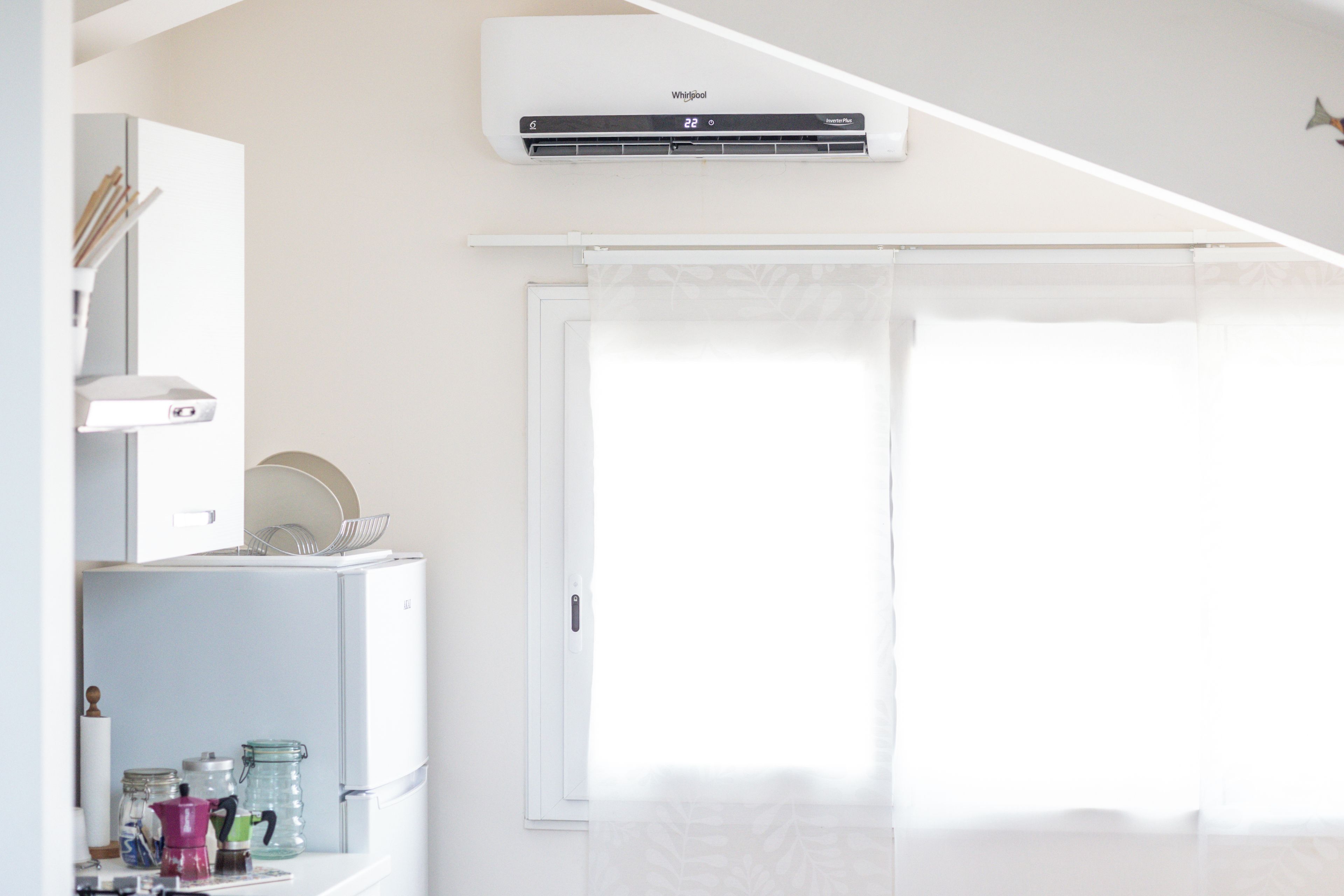 Eine moderne Küche mit integrierter Klimaanlage, einem Kühlschrank und einem Fenster mit weißer Rolljalousie.
