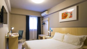 Et hotelværelse med seng, skrivebord, stol og et fjernsyn på væggen.