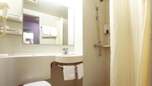 Et badeværelse med toilet, vask, spejl, bruser og et håndklædestativ.